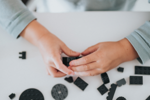 Small kid playing with black and grey legos on a white table.