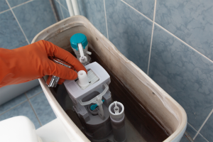 Person with orange gloves replacing parts in toilet tank because of toilet running problem. 