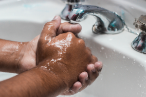 Black person washing their hands in a sink with chrome faucet.