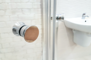 A close up of a glass shower door with a silver knob in a white bathroom.