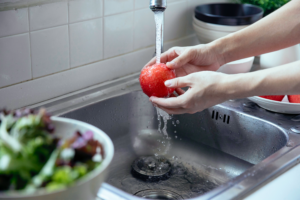 White person washing apple in silver kitchen sink with water.